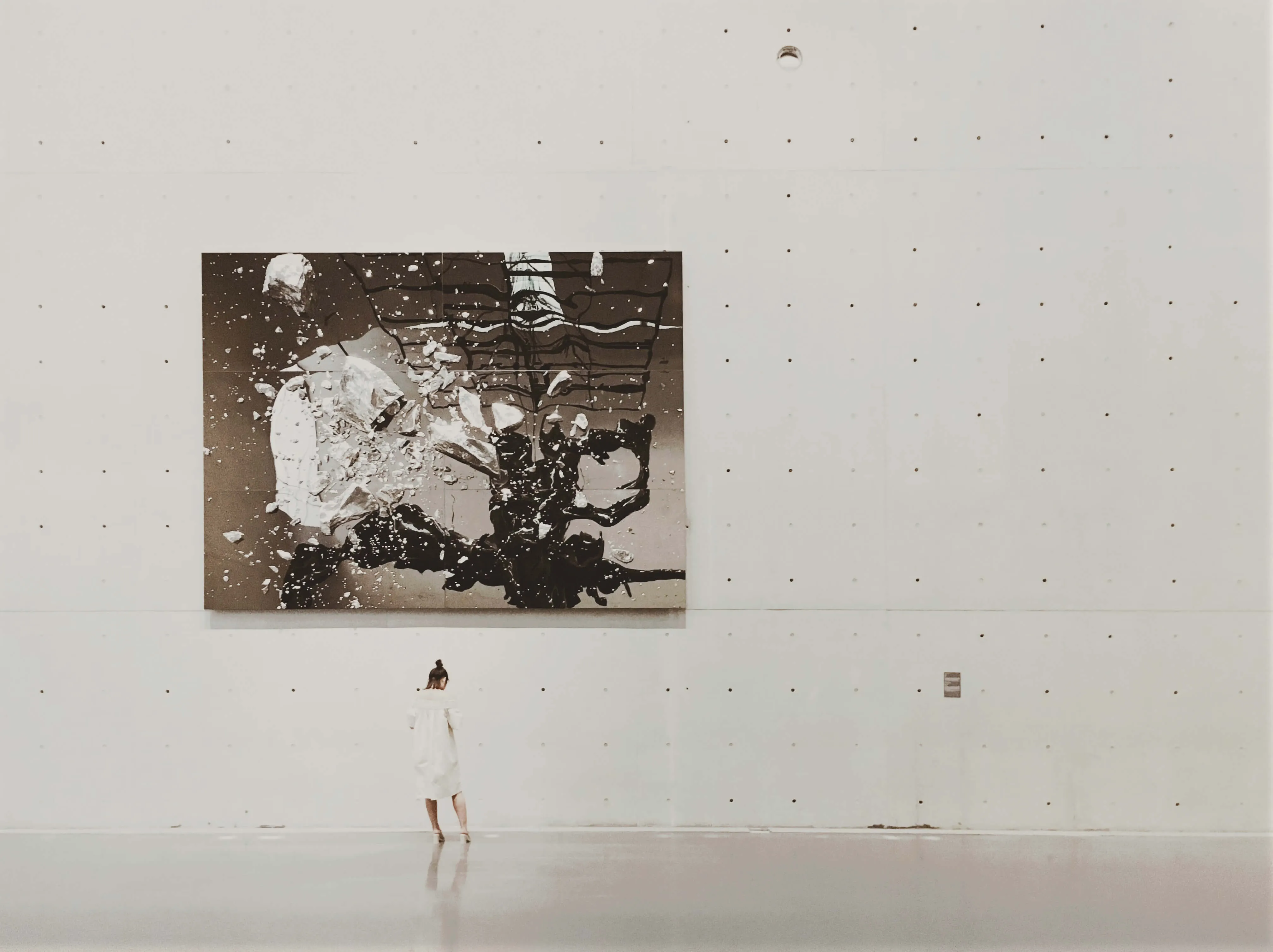 Person standing alone in a vast art gallery contemplating a large abstract painting, symbolizing the careful selection and curation process of choosing exceptional founders to back