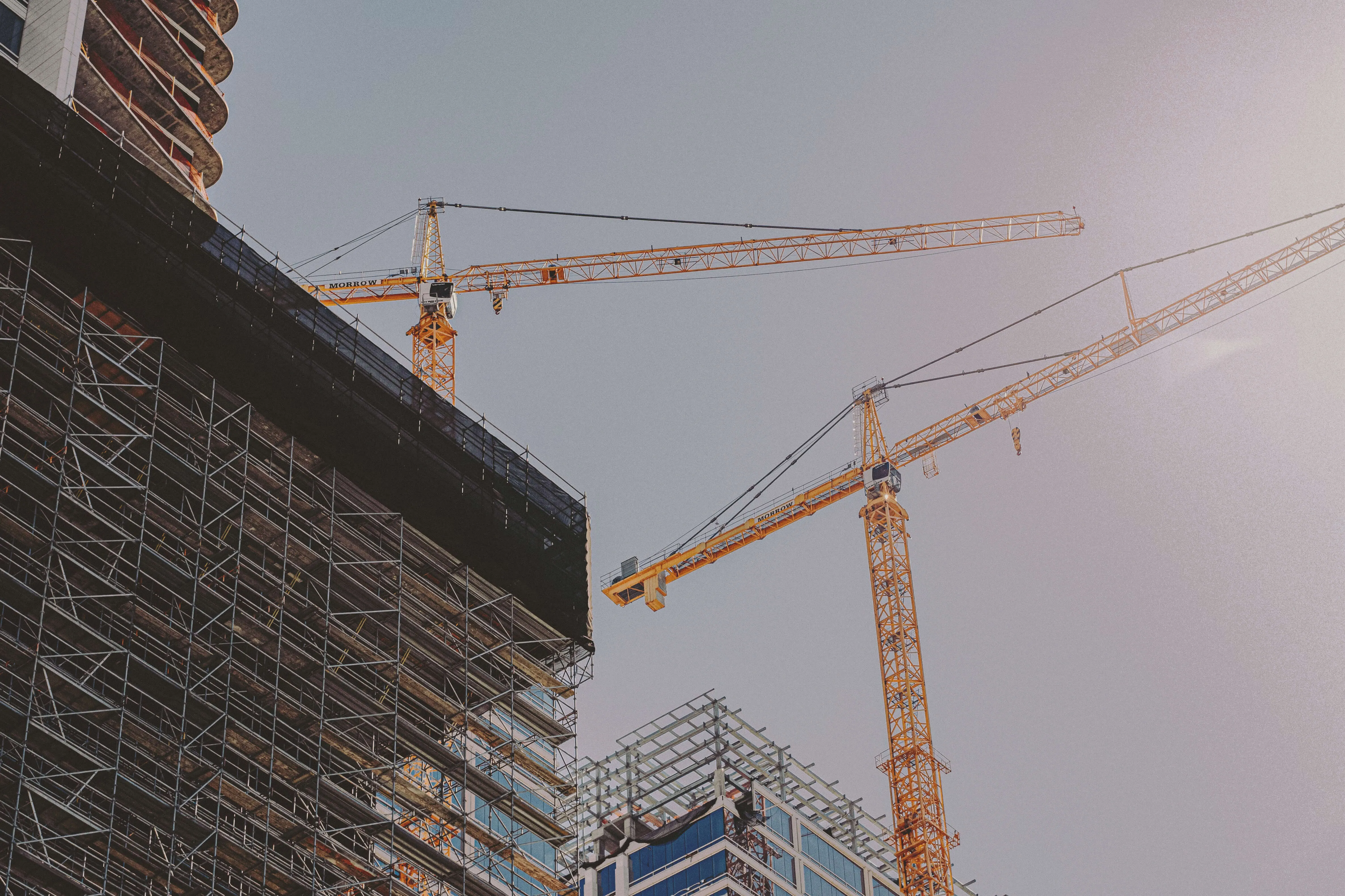 Construction cranes towering over a building site with scaffolding, representing the audacious force and intensity required to move mountains and clear paths for extraordinary achievements