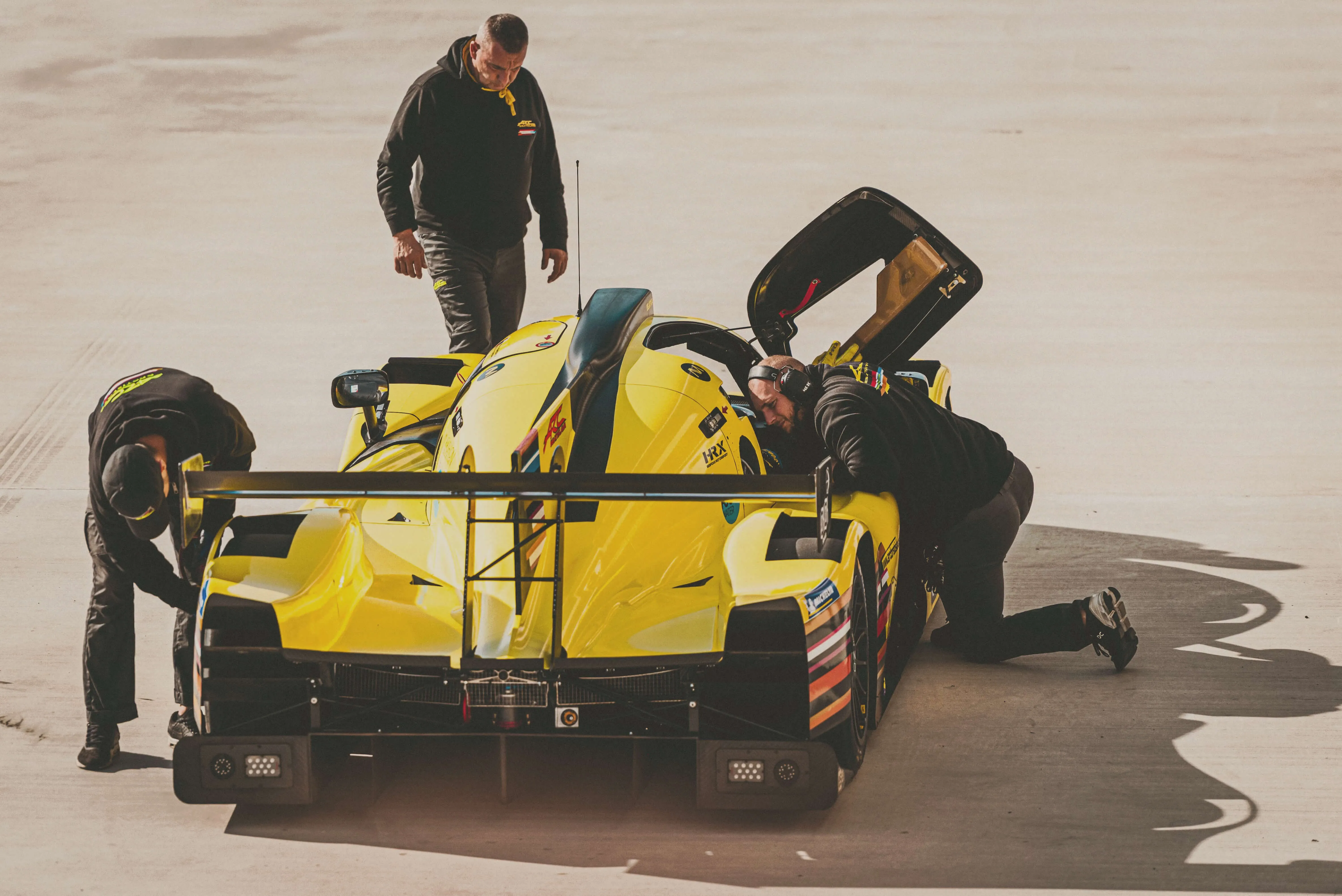 Racing team mechanics working together to optimize a high-performance race car, demonstrating how the highest impact comes from helping exceptional talent build extraordinary teams around them